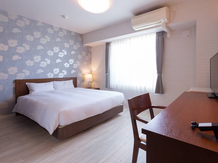 Une chambre d’hôtel équipée d’un lit, d’un bureau, d’une chaise, d’un climatiseur et d’une fenêtre avec des rideaux.