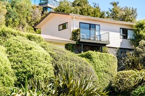 Ein modernes, zweistöckiges Haus mit Balkon, umgeben von üppigem Grün.