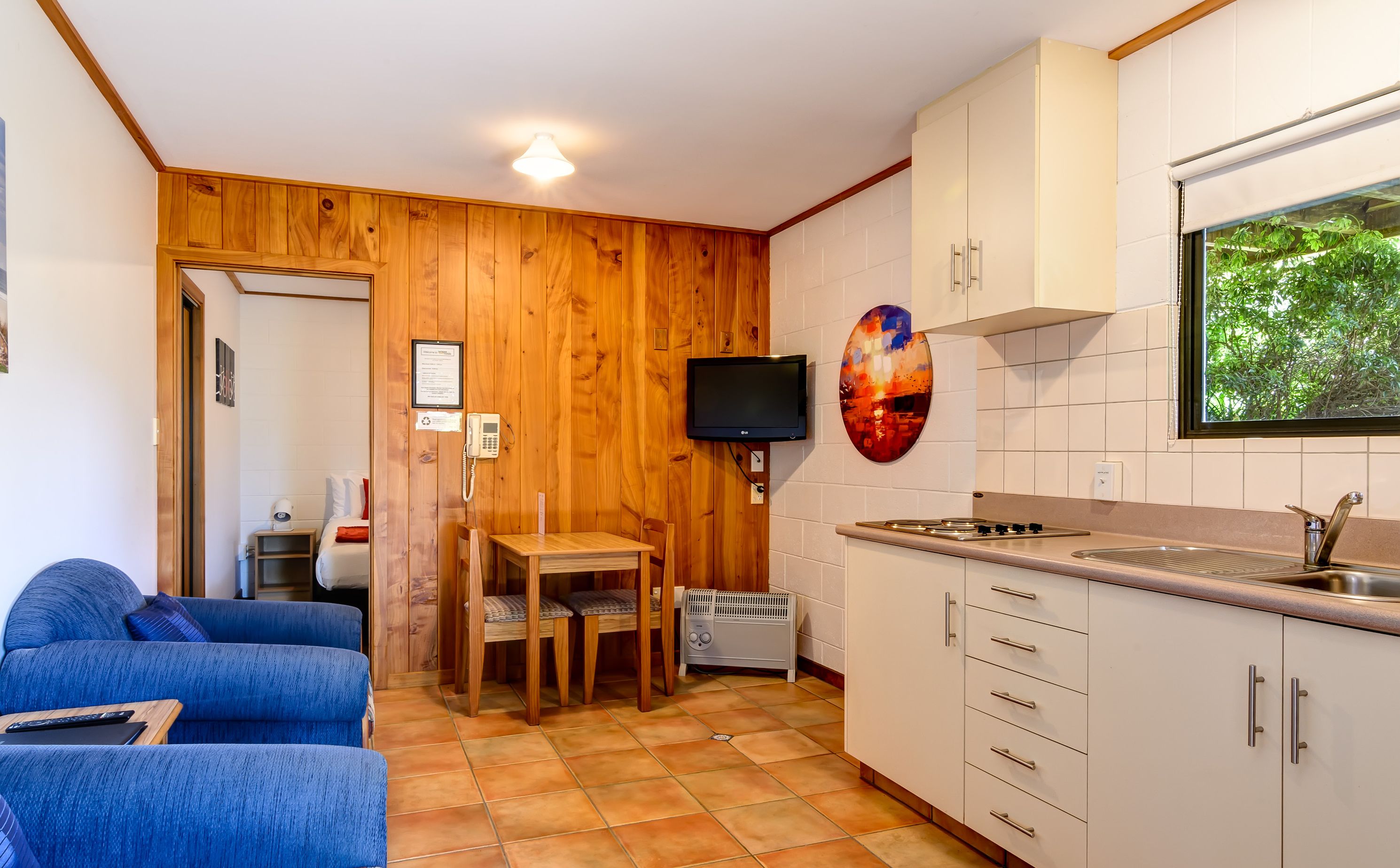 A compact kitchen with wooden walls, a dining area, and a living room with a blue sofa.