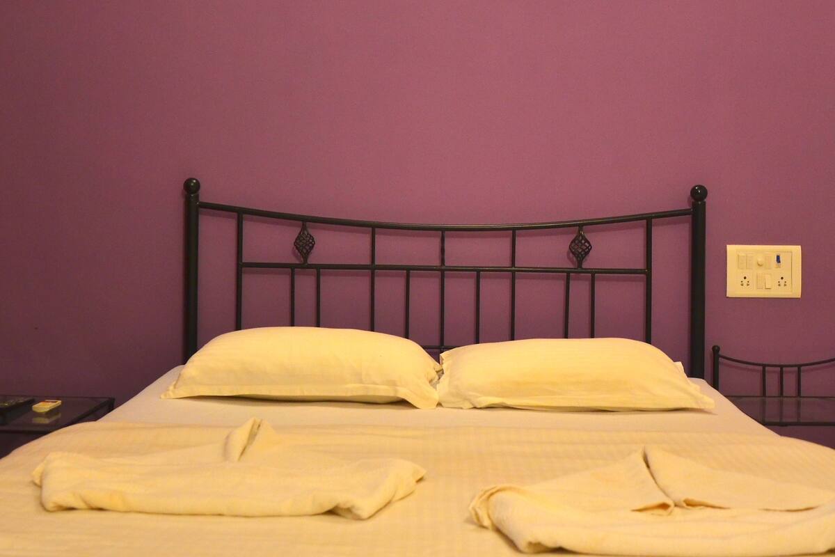 A bed with a headboard, a painting above it, and a light fixture on the wall.