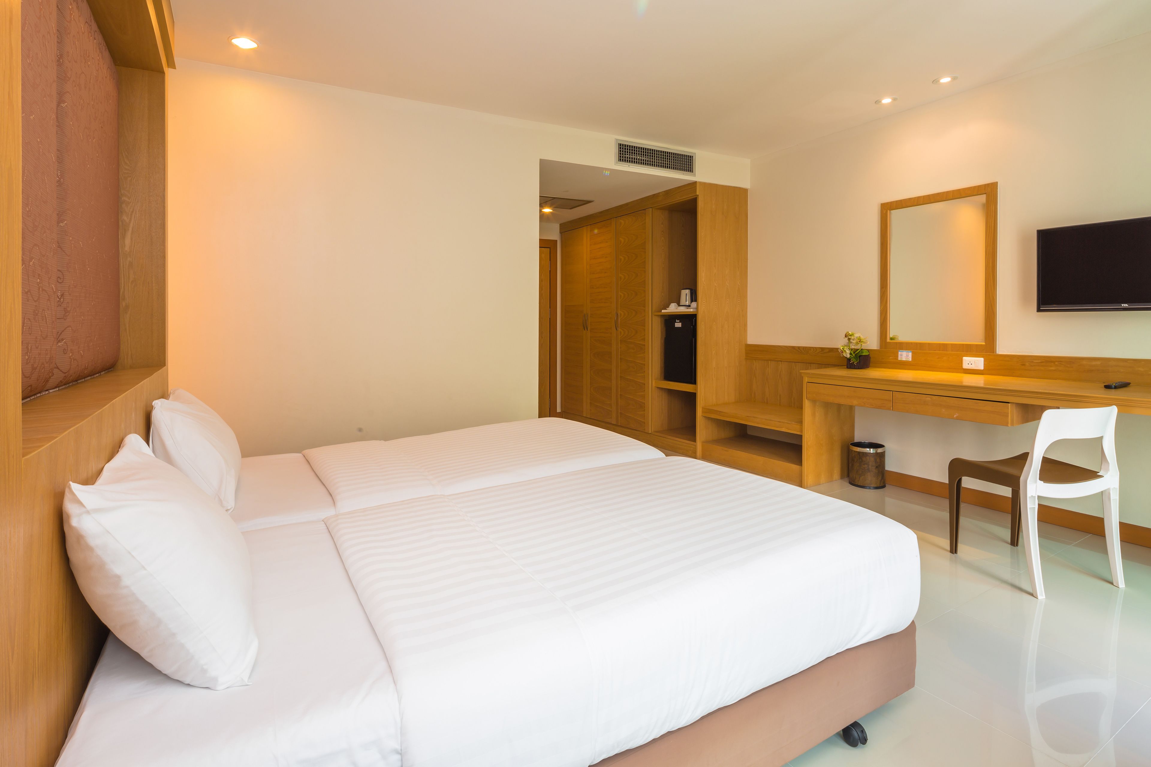 A hotel room with a large bed, a wooden desk, a chair, a TV, and a wardrobe.