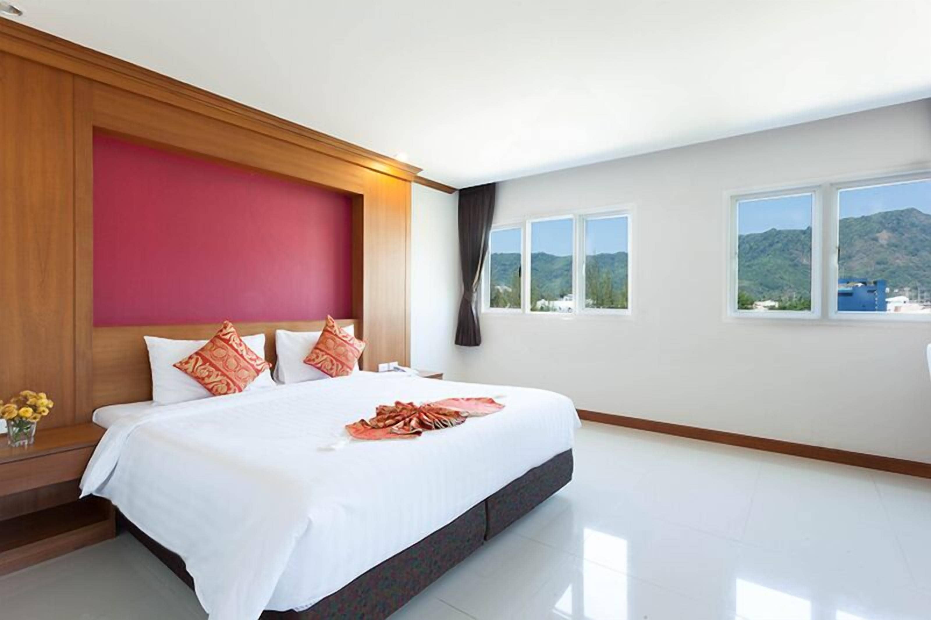 A large bed with white bedding, a wooden headboard, and a view of mountains through the windows.