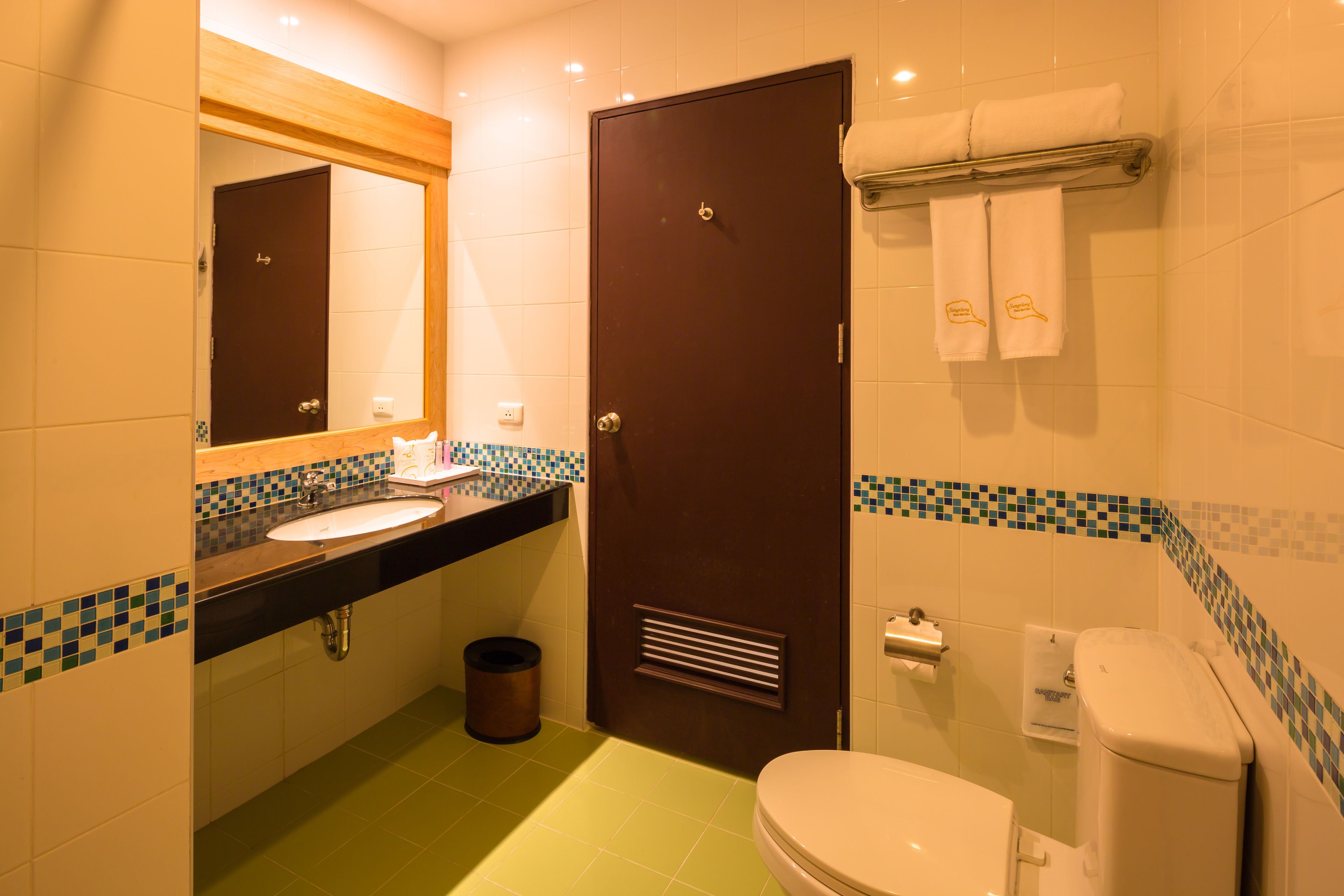 Un baño con lavamanos, espejo, inodoro y cubo de basura.