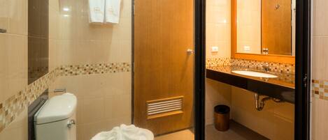 Un baño con inodoro, lavamanos, espejo y paredes de azulejos.