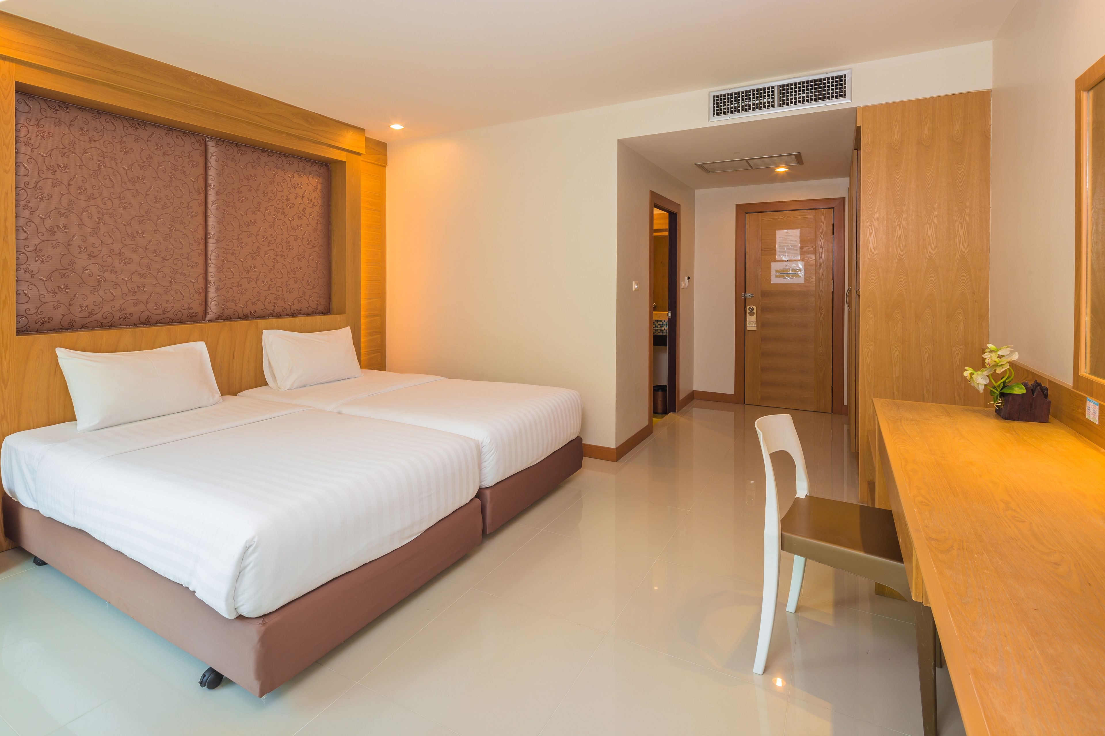 A hotel room with a double bed, a wooden headboard, a desk with a chair, and a mirror.