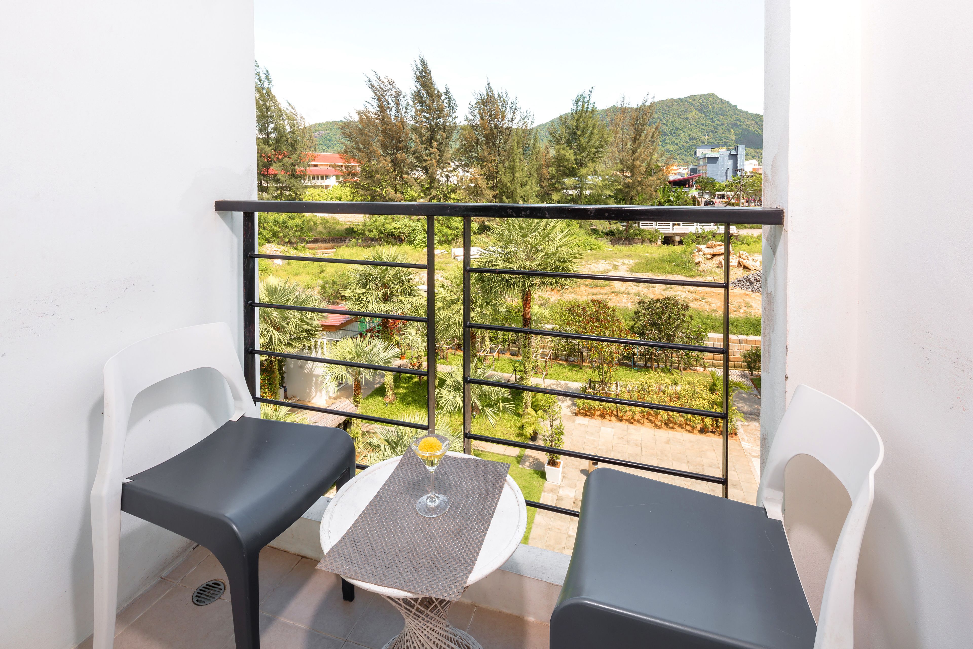 A balcony with two chairs and a table, overlooking a garden and buildings.