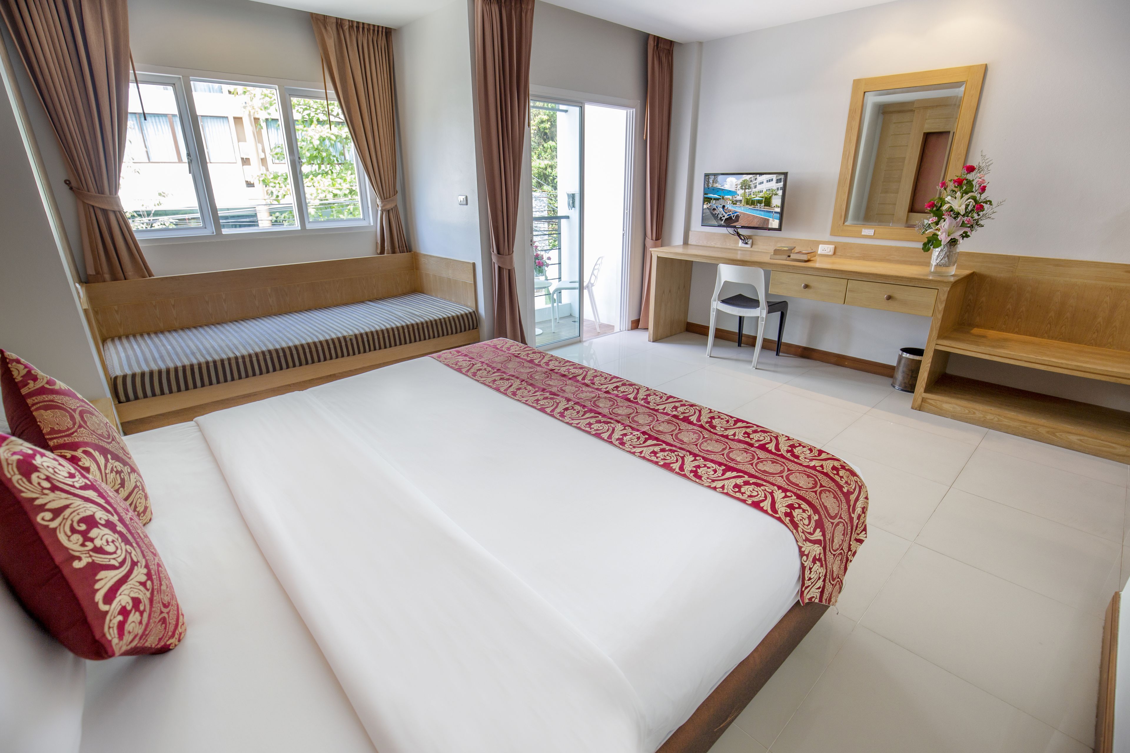 A hotel room with a large bed, a desk, a chair, a bench, a mirror, and a view of the outdoors.