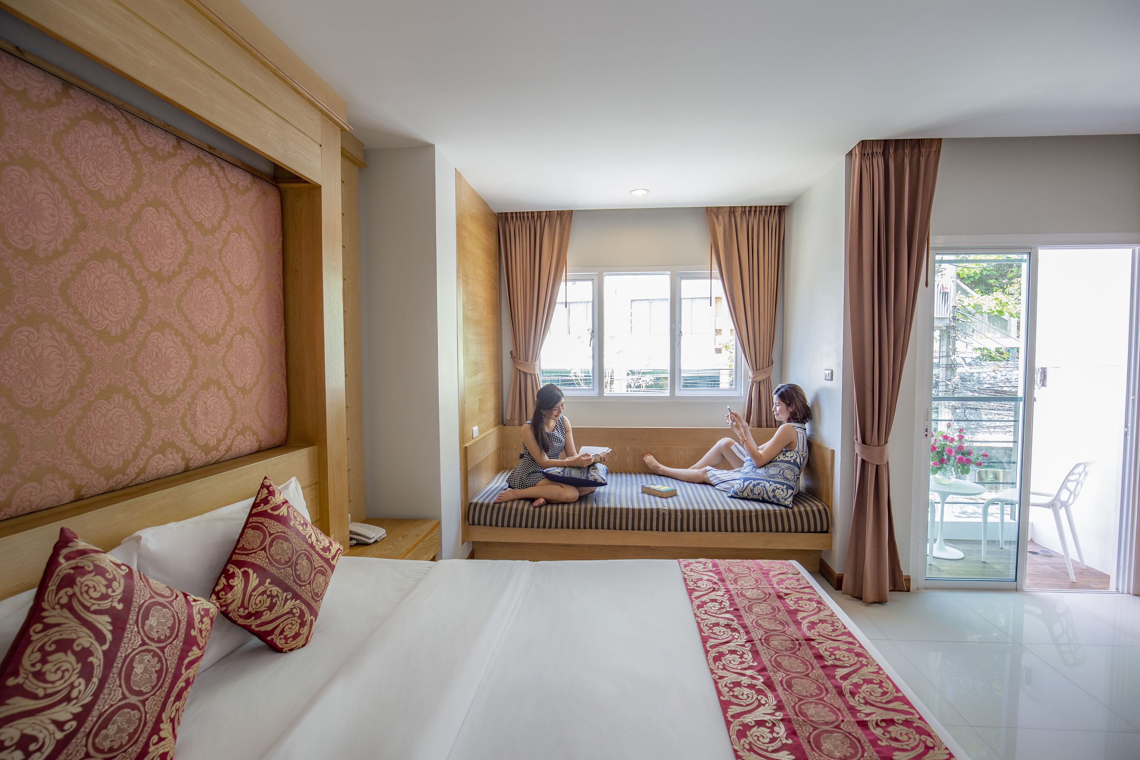 A hotel room with a large bed, two bedside tables, a window with curtains, and a balcony with a table and chairs.