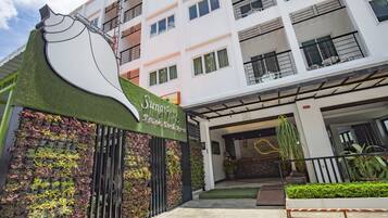 Entrada de hotel com jardim vertical verde, uma placa com a inscrição "Sunas" e um edifício moderno com varandas.