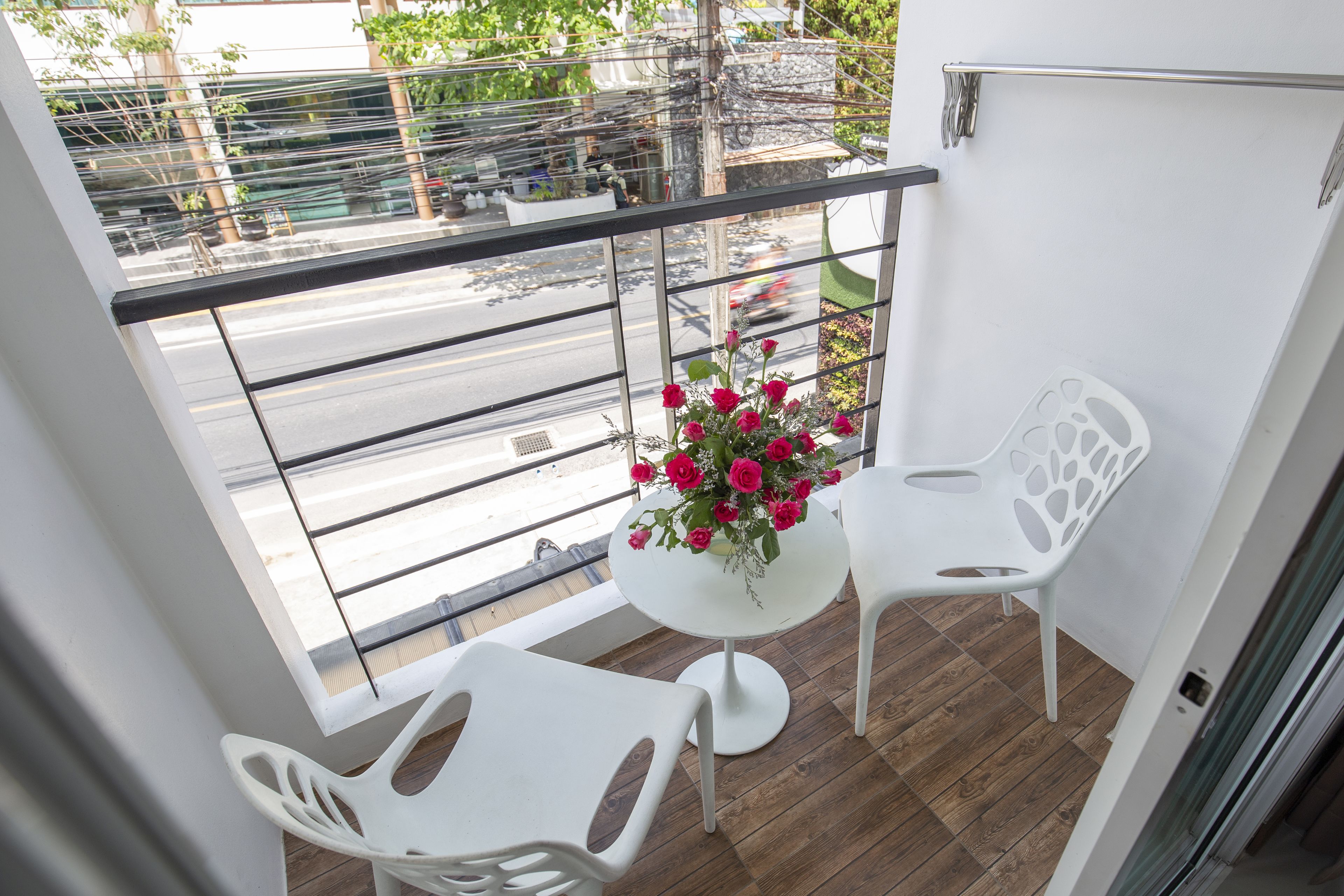 A balcony with a white table, two white chairs, and a vase of pink flowers.