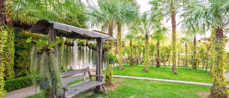 A wooden bench with a metal frame, surrounded by lush greenery and palm trees.
