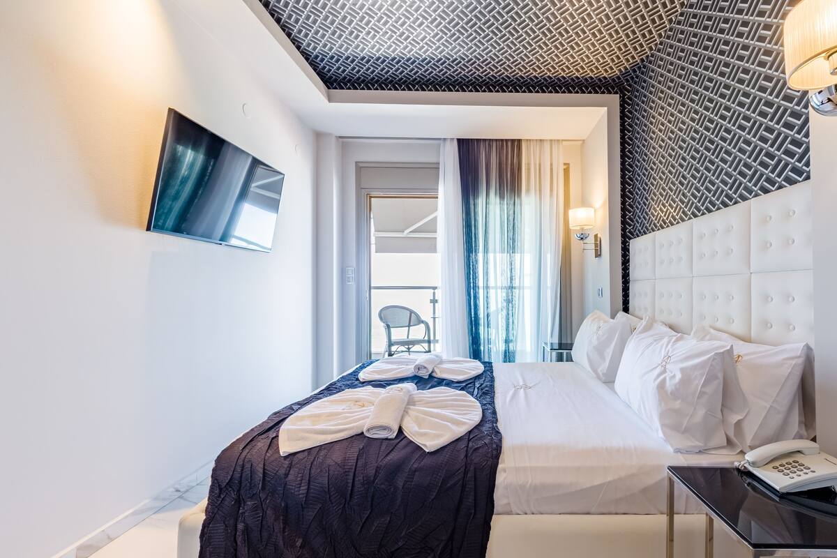 Habitación de hotel con cama, mesita de noche con teléfono, televisor montado en la pared y vista al balcón exterior.