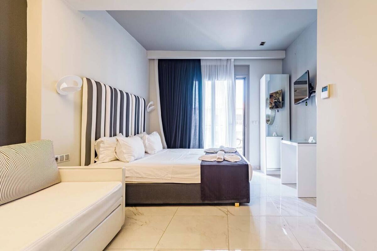 Una habitación de hotel moderna con cama, sofá, escritorio y un ventanal con cortinas.