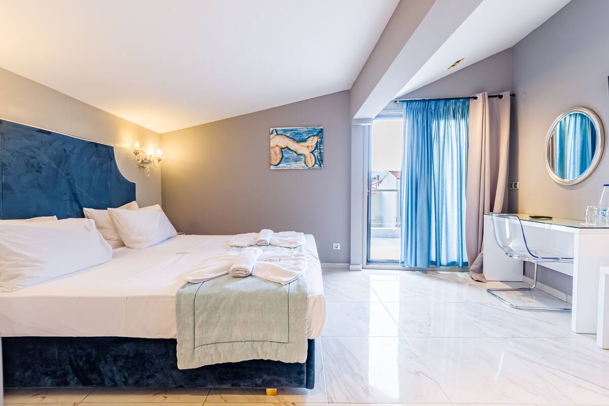 Una habitación de hotel moderna con una cama grande, un escritorio con silla, y vistas a través de una puerta de cristal.