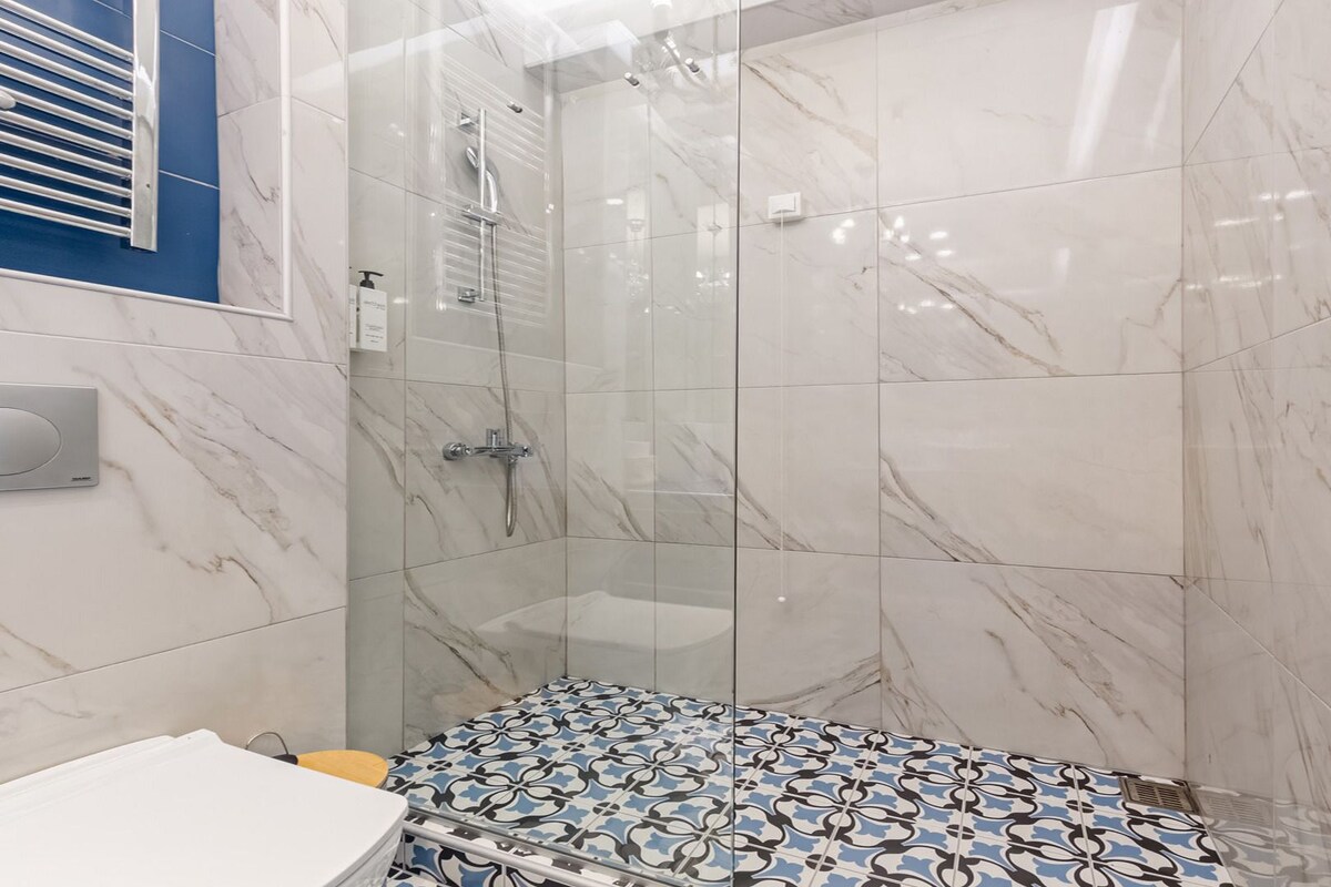Un baño moderno con ducha, baldosas de mármol, un lavamanos blanco y un suelo estampado.