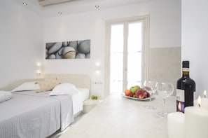 A hotel room with a bed, a dining table with fruit and wine glasses, and a painting on the wall. - Ostria Hotel (Naxos)