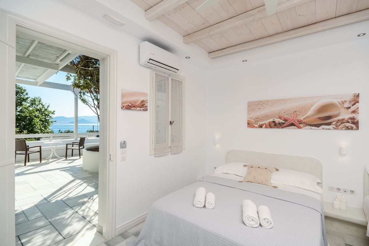 A bedroom with a bed, a nightstand, and a window overlooking a patio with outdoor furniture.
