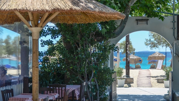 Un restaurante frente al mar con terraza, una sombrilla de paja y vistas a la playa y al océano.