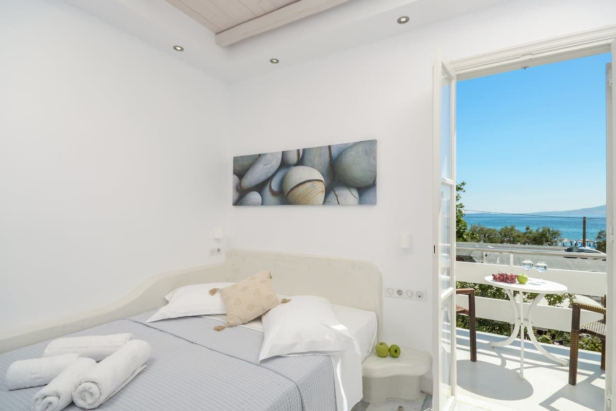A bedroom with a bed, pillows, a painting, a nightstand, and a balcony with a table and chairs.