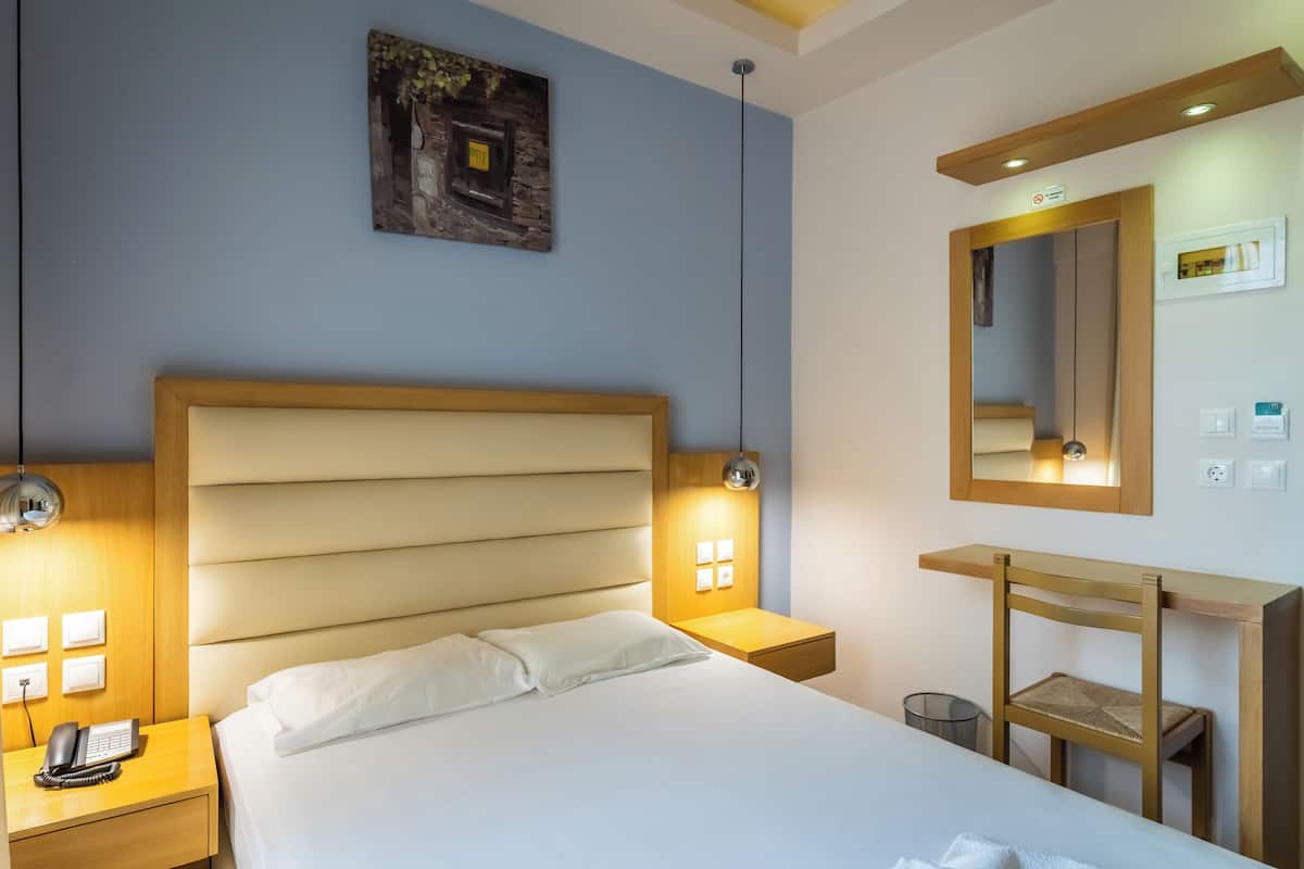Una habitación de hotel con una cama grande, lámparas de noche, una mesita de noche de madera, un escritorio con una silla y un espejo montado en la pared.