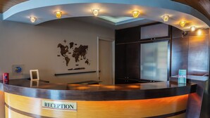 Un mostrador de recepción con un cartel que dice 'RECEPTION', un mapa mundial en la pared y una pantalla digital.