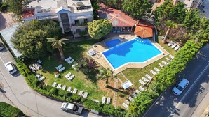 Vista aérea de un hotel con piscina, sillas de descanso y zona de estacionamiento.