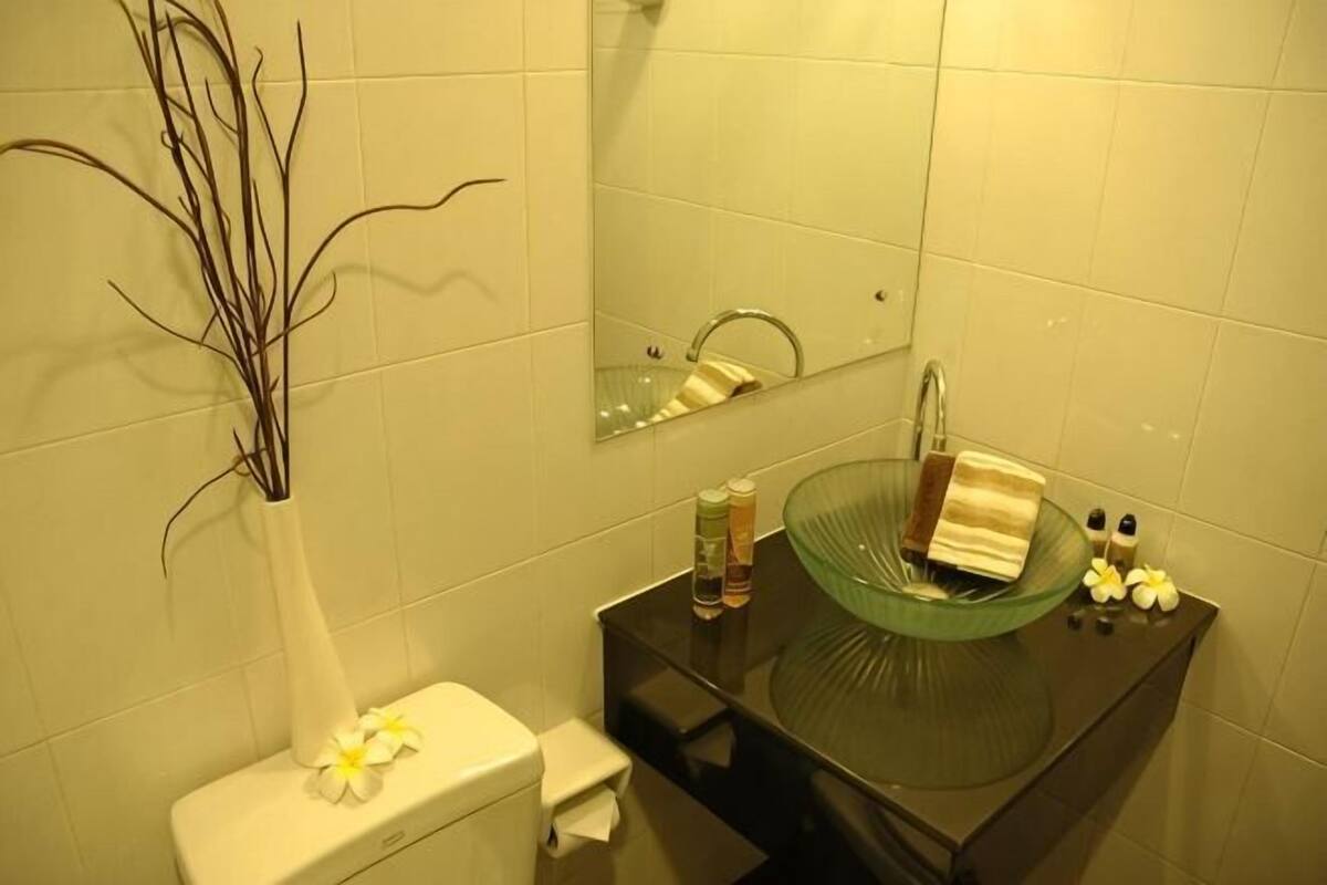 A bathroom with a toilet, a glass sink, a mirror, and a vase with a flower.