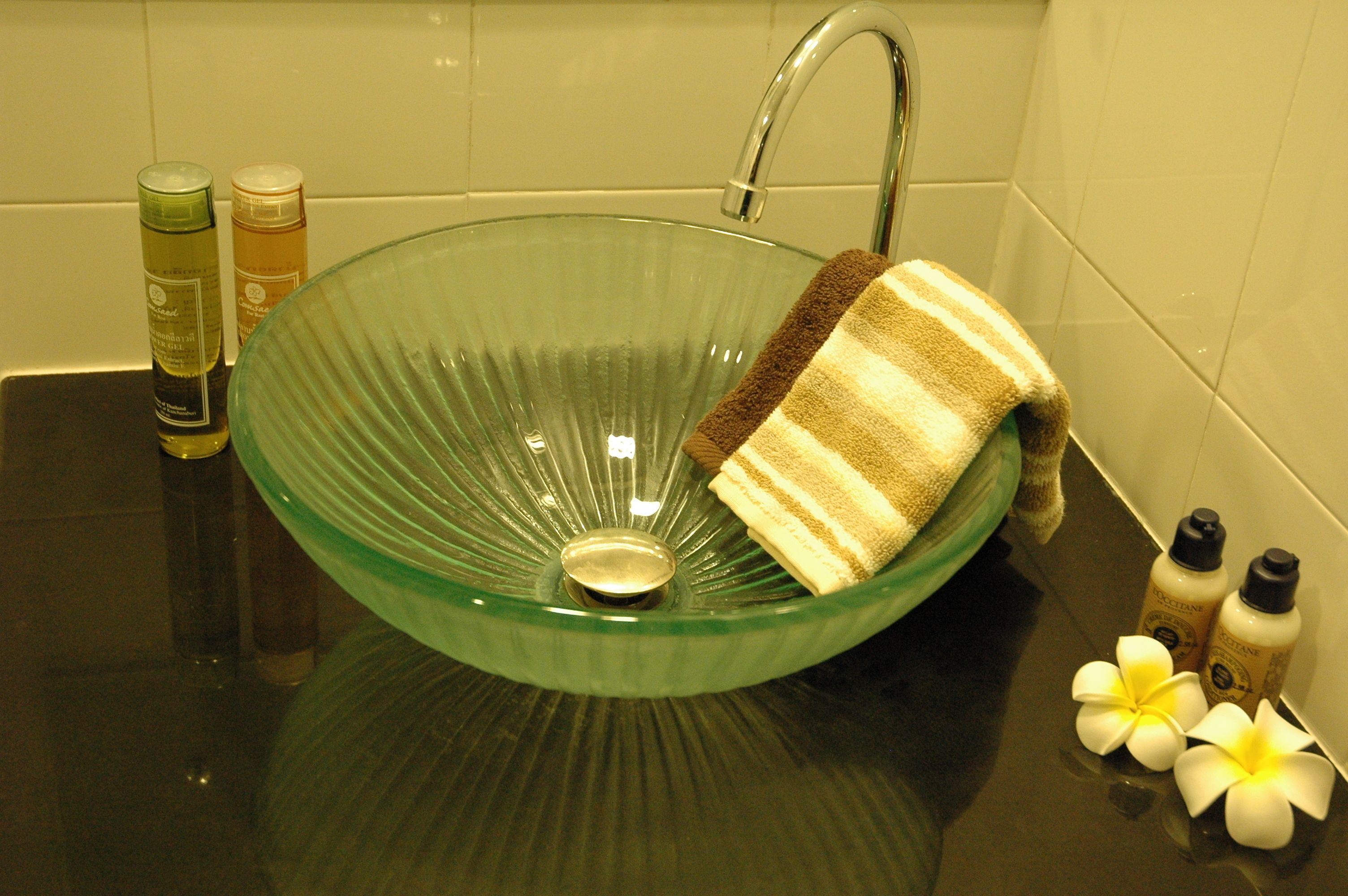Un lavabo de vidrio verde con una toalla y artículos de aseo.