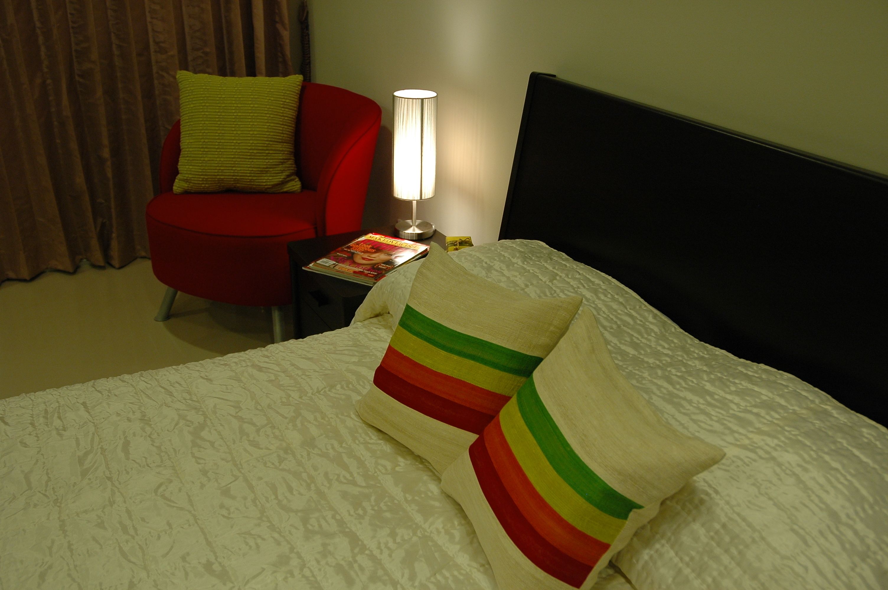 A hotel room with a bed, a red armchair, a nightstand with a lamp, and a magazine.