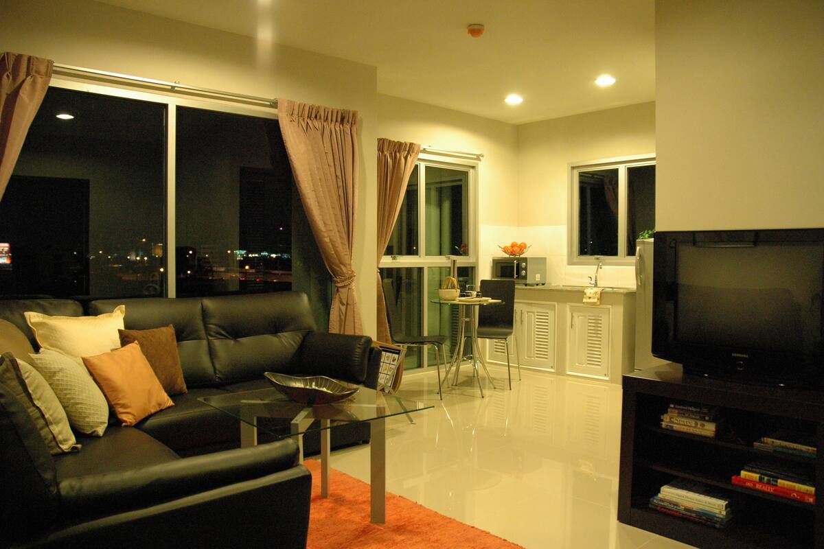 A modern living room with a black leather sofa, a glass coffee table, and a flat-screen TV.