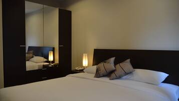 A hotel room with a large bed, a nightstand with a lamp, a mirror, and a wardrobe.