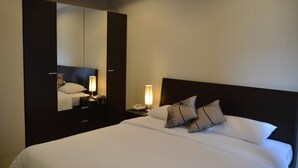 Et hotelværelse med en stor seng, et natbord med en lampe, et spejl og et sengebord med en telefon.