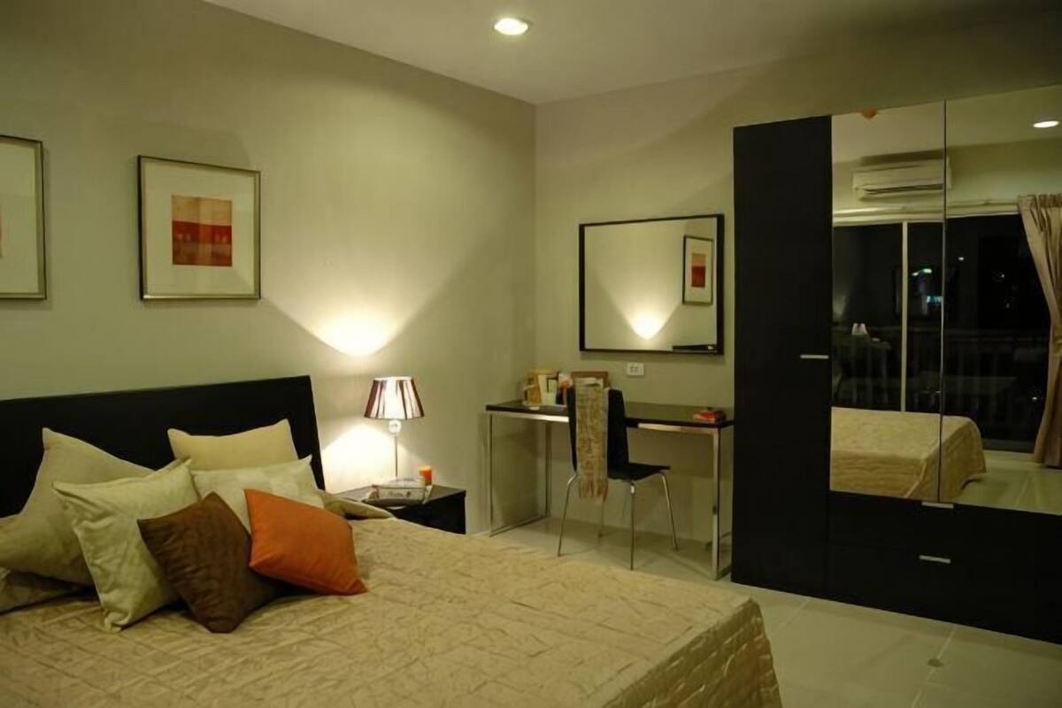 A bedroom with a bed, bedside table, desk, chair, and a large mirror.