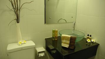 Une salle de bain équipée de toilettes, d’un lavabo en verre, d’une serviette et d’articles de toilette.