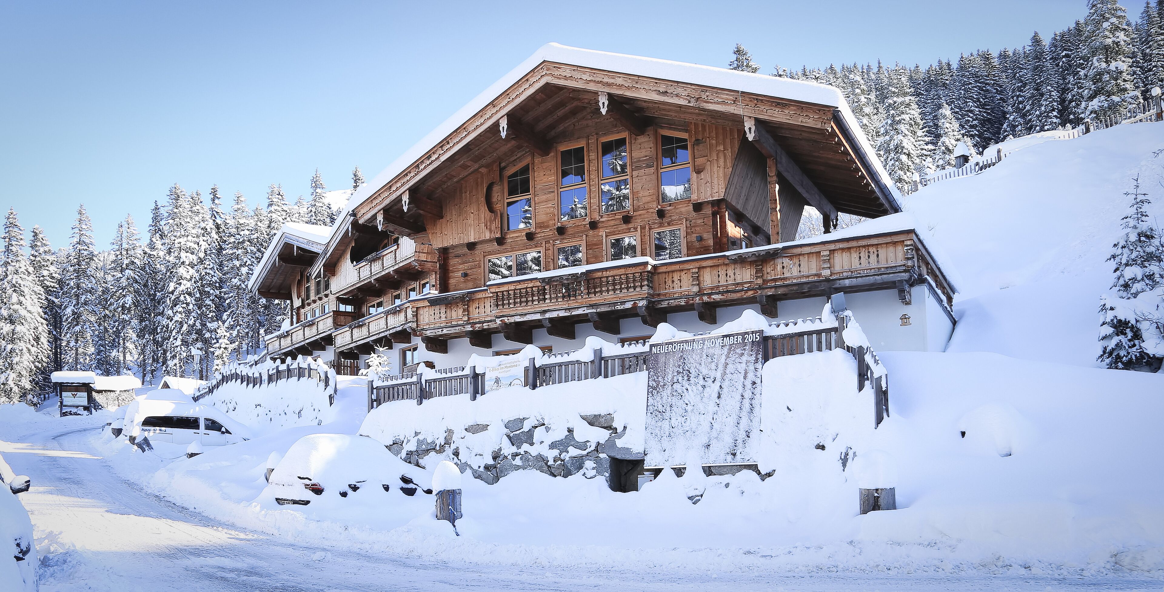 A wooden chalet with a balcony, surrounded by snow-covered trees and a clear sky.