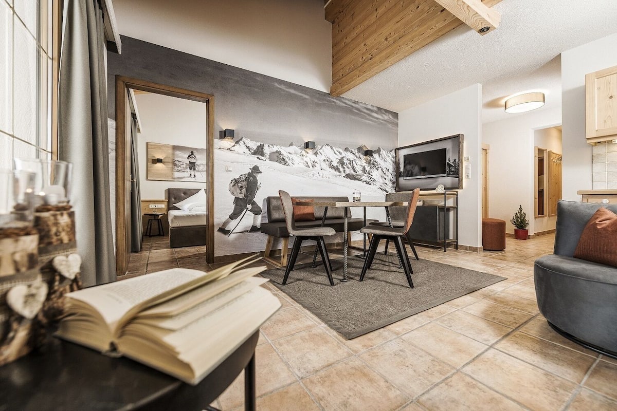 A modern living room with a dining area, a television, and a mountain-themed wall mural.