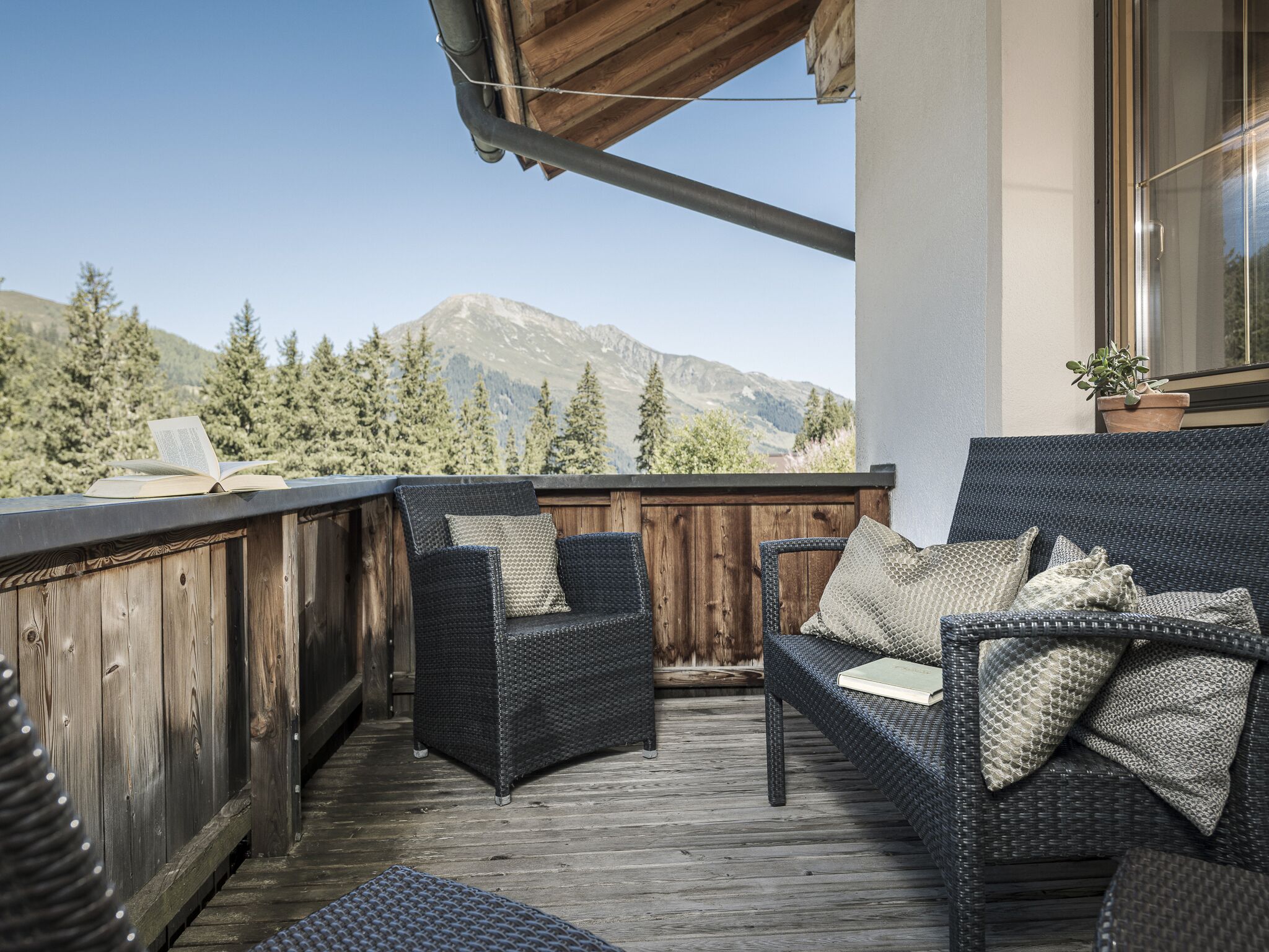 Eine Holterrasse mit Korbmöbeln, Blick auf Berge und einem Blumentopf.