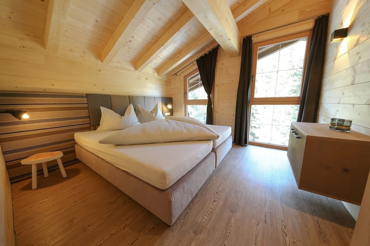 A wooden cabin bedroom with a bed, bedside table, and a small stool.