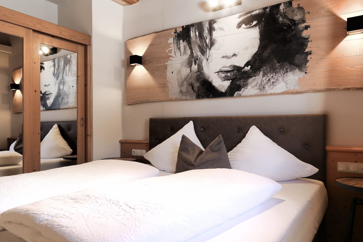 A neatly made bed with white linens and a large abstract painting above it.