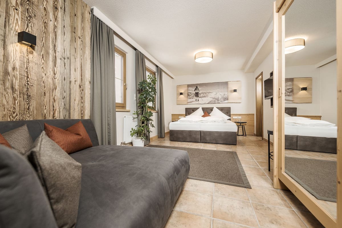 A modern hotel room with a large bed, a sofa, a mirror, and a view of the outdoors.