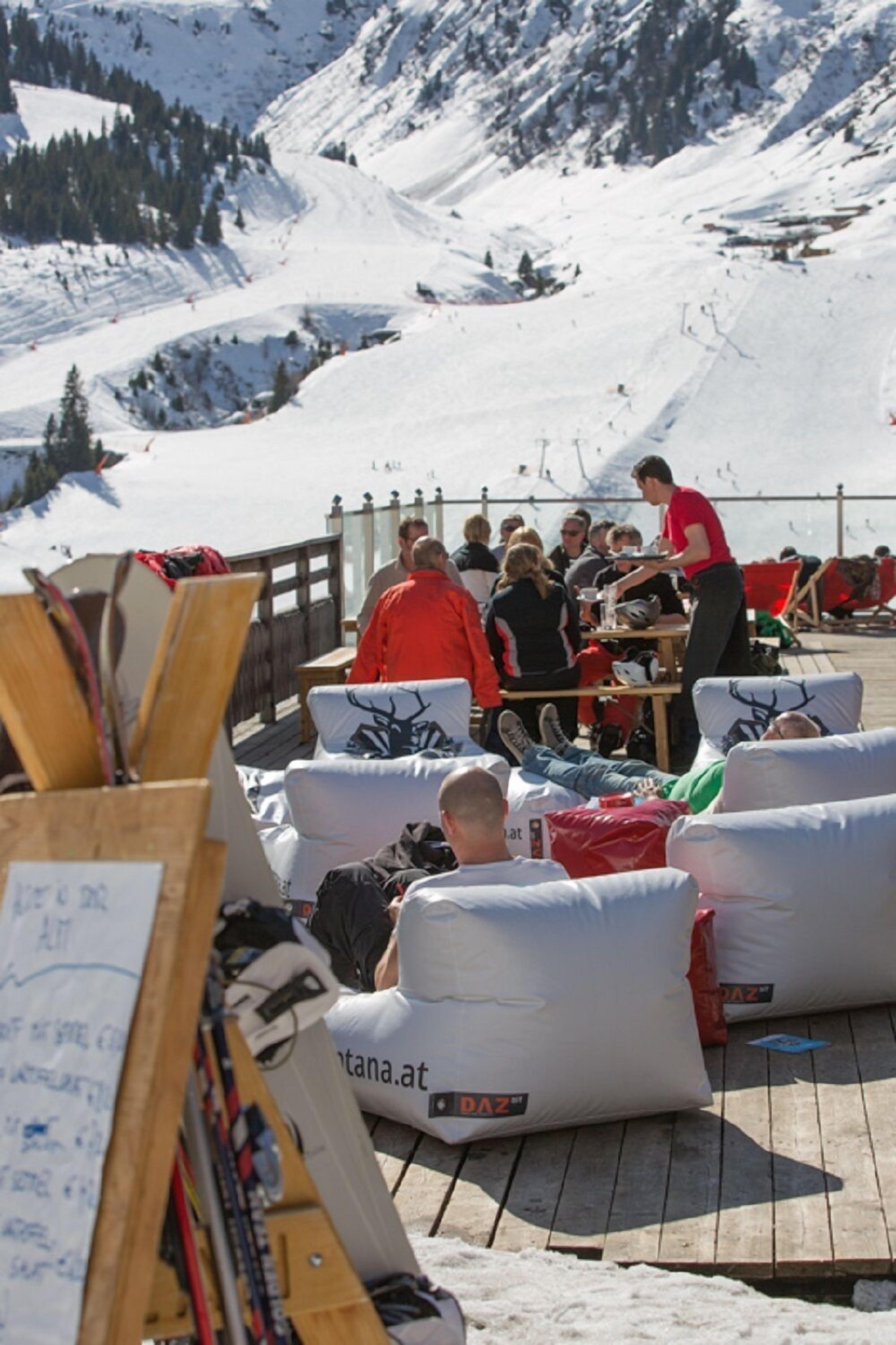A group of people seated on a wooden deck with snow-covered mountains in the background.