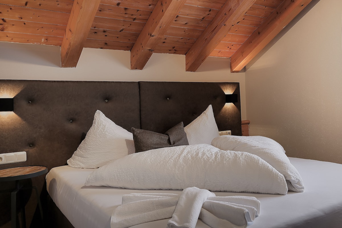 A neatly made bed with white linens and pillows, a wooden headboard, and a bedside table with a lamp.