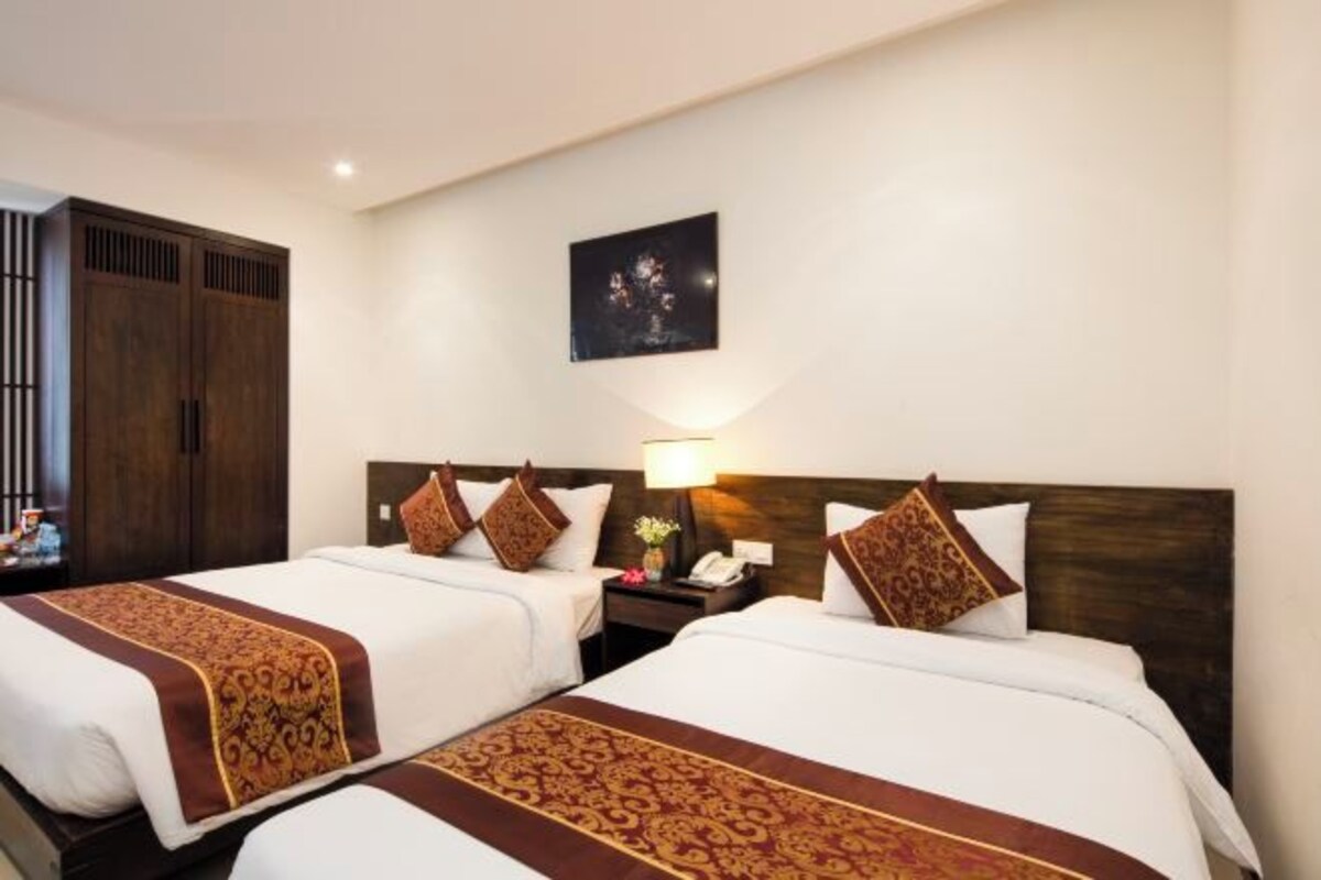 A hotel room with two beds, a wooden wardrobe, a nightstand with a lamp, and a framed picture on the wall.