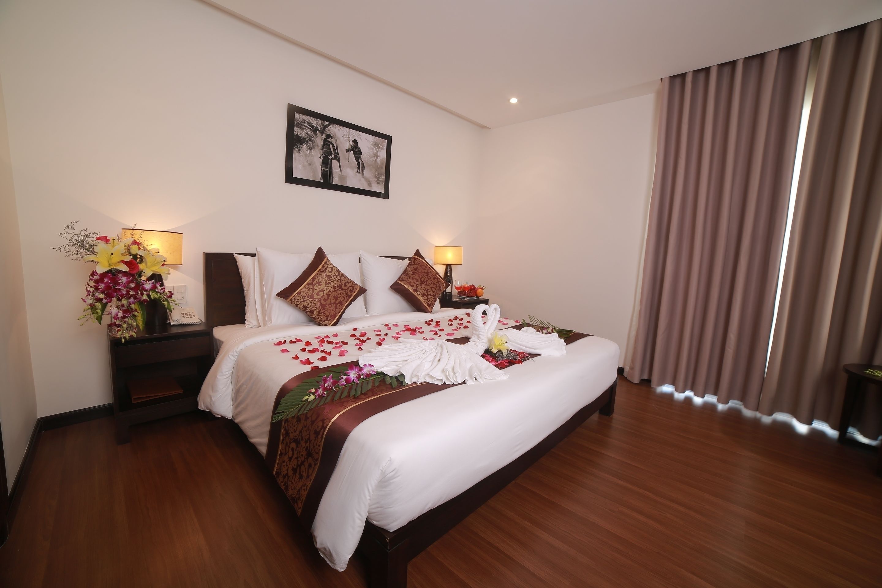 A hotel room with a large bed, two bedside tables with lamps, a framed picture on the wall, and a window with curtains.