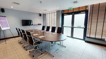 A conference room with a large table, chairs, a projector screen, and a large window with blinds.
