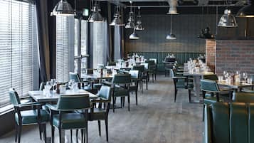 A restaurant with multiple tables and chairs, large windows, and hanging pendant lights.