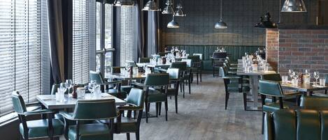Un restaurante con varias mesas y sillas, amplias ventanas y lámparas colgantes.