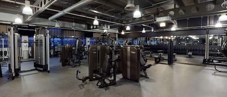 Une salle de sport équipée de divers appareils d’exercice, dotée de grandes fenêtres et d’un éclairage de style industriel.