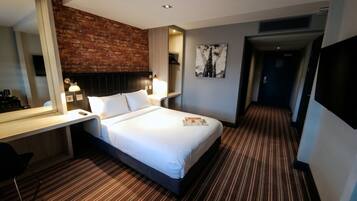 Een hotelkamer met een bed, een bureau, een spiegel, een aan de muur hangend schilderij en een deur naar een andere kamer.