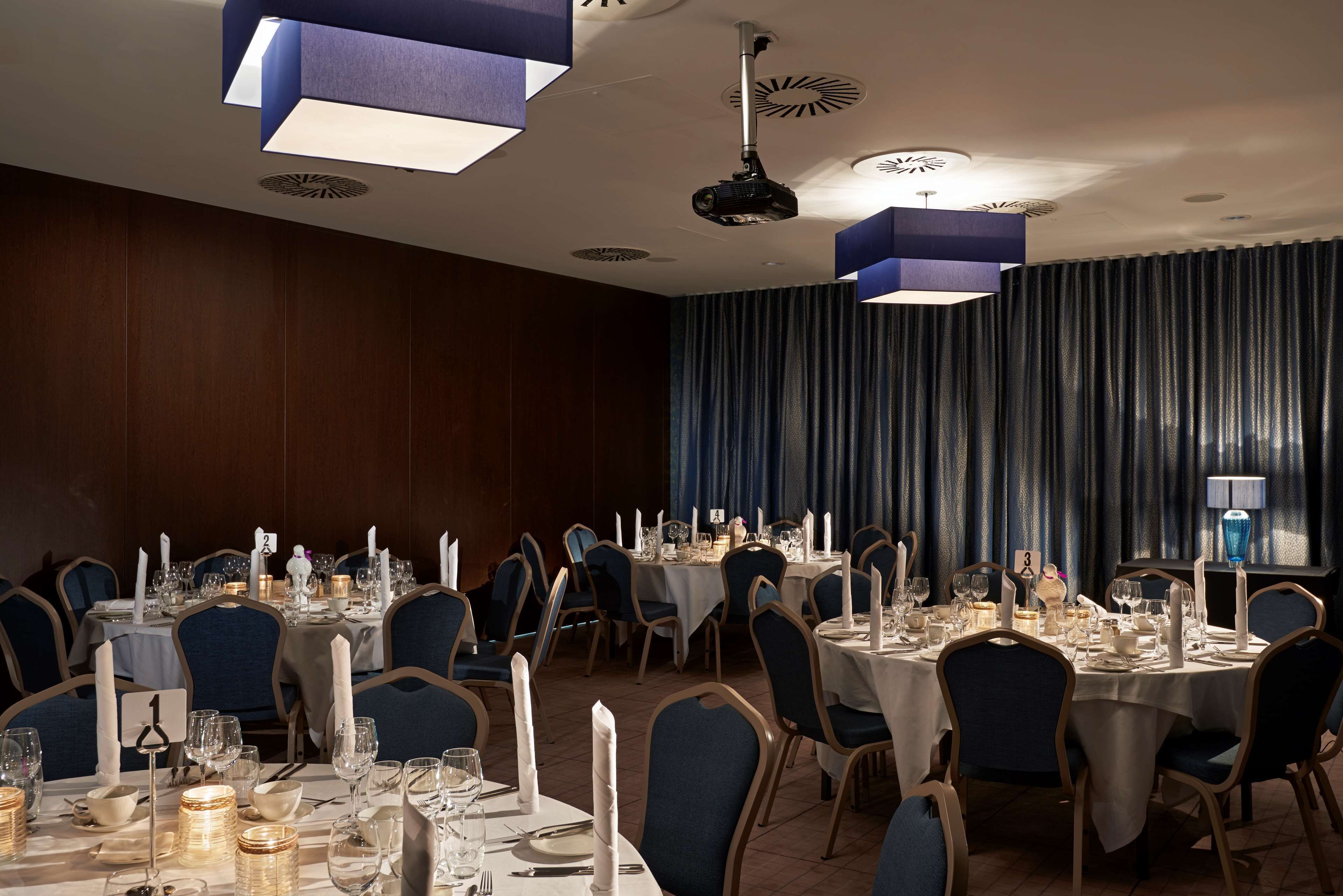 A banquet hall with round tables set for dining, blue chairs, and white tablecloths.